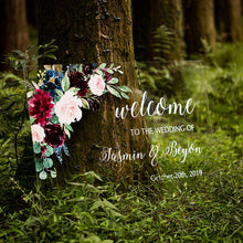 Load image into Gallery viewer, A clear acrylic wedding sign adorned with lovely florals is set against a backdrop of lush greenery, creating a striking visual contrast. The sign reads "Welcome to our wedding" in elegant script font, with the names and wedding date of the happy couple featured prominently below.