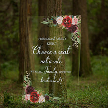 Load image into Gallery viewer, Against a backdrop of lush greenery, a clear acrylic wedding sign is elegantly adorned with beautiful florals. The sign reads "Friends and family kindly choose a seat not a side we’re all family one the knot if tied," written in a script font that exudes romance.