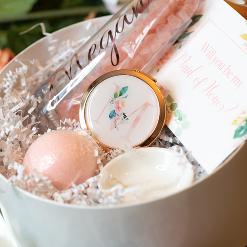 A dusty pink monogram compact mirror with a pretty floral letter on top, folded in half to reveal both a regular and a 2x magnifying mirror. It's a perfect gift for girls, bridesmaids, and women, and is small enough to fit in any purse or makeup bag.