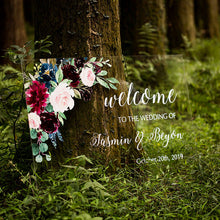 Load image into Gallery viewer,  A clear acrylic wedding sign adorned with lovely florals is set against a backdrop of lush greenery, creating a striking visual contrast. The sign reads &quot;Welcome to our wedding&quot; in elegant script font, with the names and wedding date of the happy couple featured prominently below.
