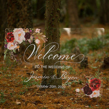 Load image into Gallery viewer, Set amidst a lush greenery background, a clear acrylic wedding sign adorned with exquisite florals is sure to captivate guests&#39; attention. The sign reads &quot;Welcome to our wedding,&quot; written in a graceful script font, with the names of the happy couple featured prominently below.
